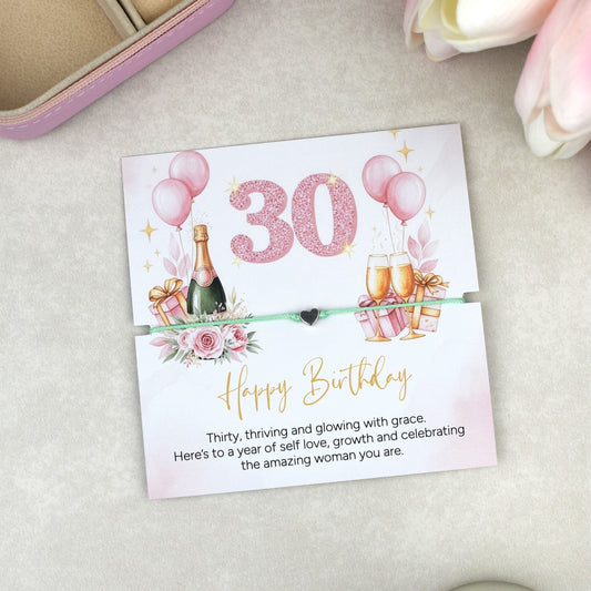 Thirty birthday wish bracelet with adjustable cord and silver heart charm, presented on a feminine illustrated 30th birthday card with balloons, gifts and champagne